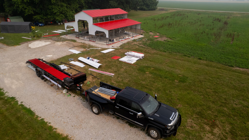 A partially assembled red-roofed steel building beside a gravel work area, photographed from above.