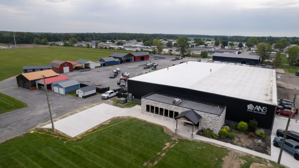 Aerial view of the ANS Steel Buildings facility with rows of display garages and sheds beside a gravel yard.
