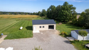 Tan metal garage with a dark roof, two windows, a white entry door, and an open garage bay beside a gravel driveway.